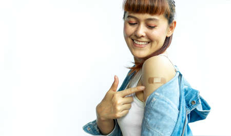Asian woman smiling using adhesive bandage plaster at arm gesture after injection vaccine on a white isolated background. Female cheerful and confident in getting vaccinated against various diseases.の写真素材
