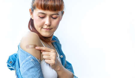 Asian woman using adhesive bandage plaster at arm gesture after injection vaccine on a white isolated background. Female confident in getting vaccinated against various diseases.の写真素材