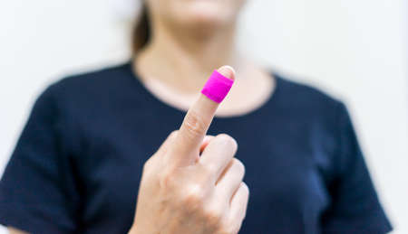Close up young woman puts a adhesive tape on her finger. Female bandage pink on injured her hand.の写真素材
