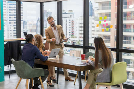 A team of business people wear face shield chatting in an office meeting room. Group businessmen and...