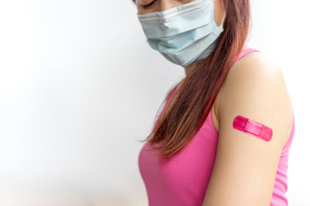 Asian woman wear face mask using adhesive bandage plaster at arm gesture after injection vaccine. Covid 19 vaccine disease preparing.の写真素材