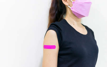 Asian woman wear face mask using adhesive bandage with pink at arm after injection vaccine. Covid 19...