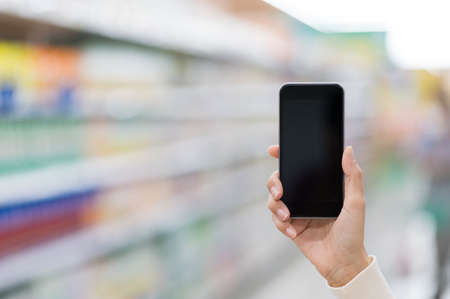 A hand female holding blank screen of smartphone on blurredâ€‹ background in supermarket.