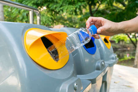 A hand female throwing empty plastic water bottle into to recycling bin at park. Environmental...
