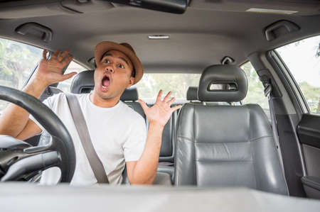 Handsome asian man with hat look outside shocked and surprised  looking in his car.の写真素材