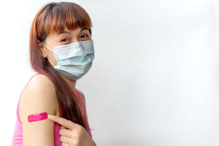 Asian woman wear face mask using adhesive bandage with pink at arm gesture after injection vaccine. Covid 19 vaccine disease preparing.の写真素材
