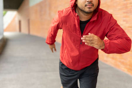 Sportsman wearing a red jacket running on the background of a brick wall stadium. Fitness man runner...