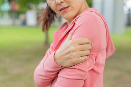 Young woman in sports outfits pink injured her upper arm during exercise in the park. Upper section of sports girl suffering from arm pain while sitting at workout. Accident from exercise concept.の写真素材
