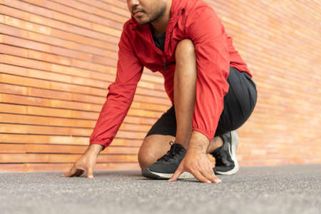 Sportsman wearing a red jacket running on the background of a brick wall stadium. Fitness man runner on urban street. Male jogging and exercise outdoor. Asian athlete man run on start at treadmill.の写真素材