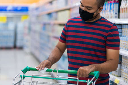 Asian man wearing medical face mask wipes shopping cart handle in supermarket for prevent  dust the spread of germs and bacteria and avoid infections corona virus. Hygiene conceptの写真素材