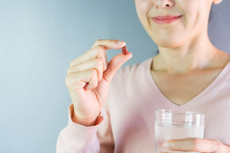 Smiling healthy young woman holding pill glass of water take medicine vitamin supplements for health...