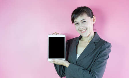 Businesswoman in suit smiling showing tablet on pink background.