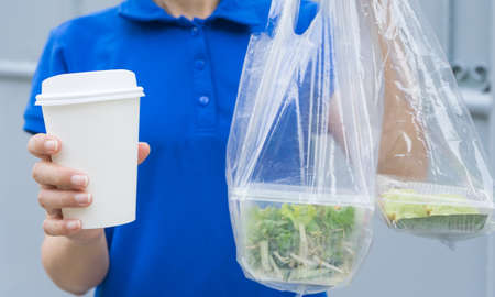 Deliverywoman in blue uniform delivered food boxes in plastic bags and coffee in paper cup to...