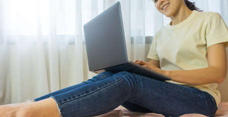 Young woman smiling using laptop on bed at home. Work from home conceptの写真素材