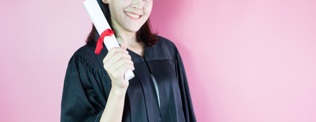 Happy graduate smiling she is in graduation cap and diploma in hand on pink background.の写真素材