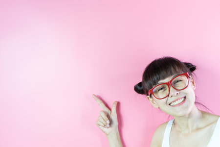 Funny woman in glasses pointing finger at copy space on pink background.の写真素材