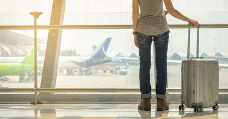 Backside female tourist wearing a hat, standing a trolley luggage is waiting to travel by plane. Travel conceptの写真素材
