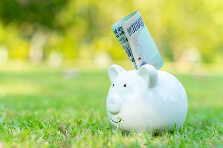 Putting Japanese yen banknote into piggy bank on green grass outdoors with copy space. Investing and saving money concept. Financial planning and money saving concept.の写真素材