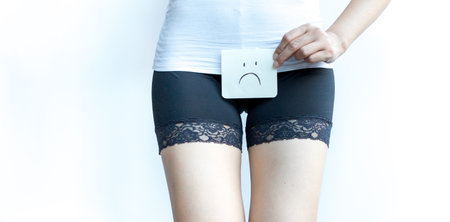 Young woman holds paper with sad above crotch on withe isolate background. Period Pain or vaginal or urinary infection female health Problem. Health Issues Concept.の写真素材