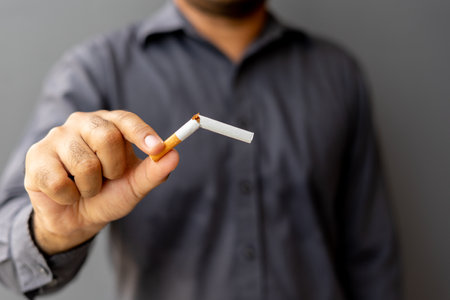 Portrait young man holding broken cigarette in hands. Happy male quitting refusing smoking cigarettes. Quit bad habit, Stop smoking cigarettes, health care concept. No smoking campaign.の写真素材