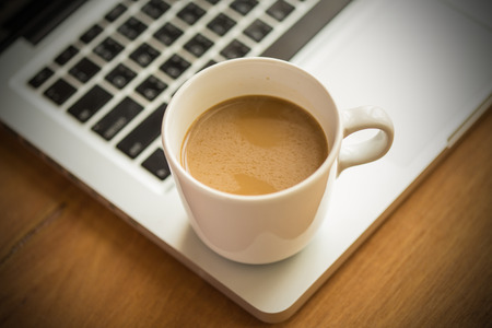 Hot latte coffee cup and laptop on wood background and texture.の写真素材