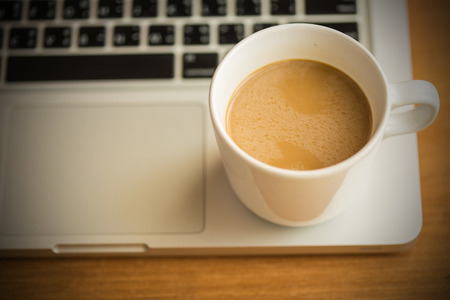 Hot latte coffee cup and laptop on wood background and texture.の写真素材