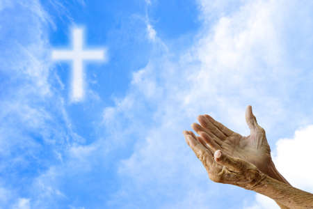 Hands of senior women praying over blurred the cross on the sky.