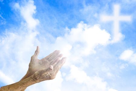 Hands of senior women praying over blurred the cross on the sky.
