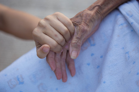 Old and young holding hands on light background, closeupの写真素材