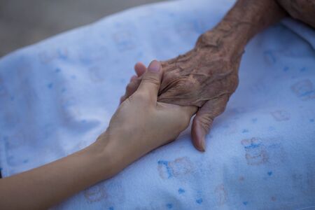Old and young holding hands on light background, closeupの写真素材