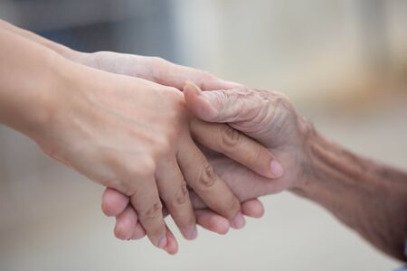Old and young holding hands on light background, closeupの写真素材