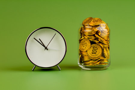 Saving gold coins in glass jars on green background, coin savings concept