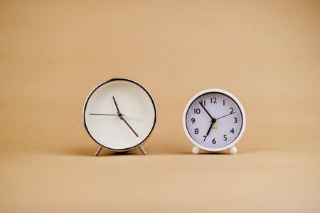 Two white alarm clocks on a beige background. Time concept.