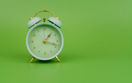 Green alarm clock photo in studio on green background. Time and work and life.の写真素材
