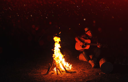 Playing acoustic guitar by the campfire and camping activities for entertainment and relaxationの写真素材