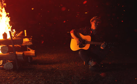 Musicians play guitars by the campfire at night, relaxing by playing music and enjoying themselves.