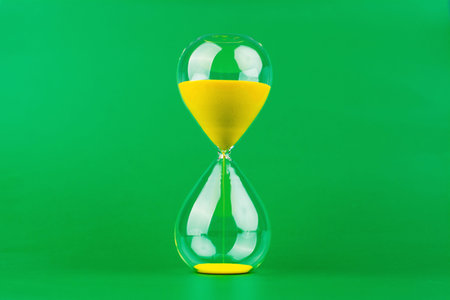 A yellow hourglass against a green background, representing the concept of working with limited time and the constraints of precious time.の写真素材