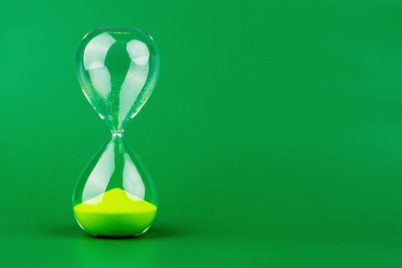 An hourglass, green on a green background, represents working with limited time and the constraints of precious time.の写真素材
