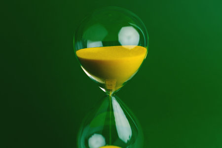 A yellow hourglass against a green background, representing the concept of working with limited time and the constraints of precious time.の写真素材