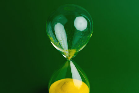 A yellow hourglass against a green background, representing the concept of working with limited time and the constraints of precious time.の写真素材