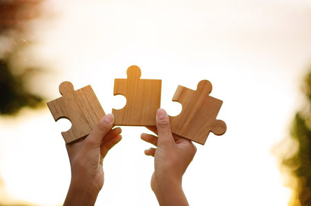 The wooden jigsaw puzzle and sparkling sunlight powerfully represent cooperation and teamwork.の写真素材