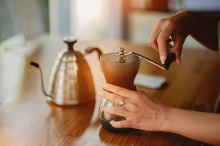 Grinding fresh coffee beans by hand and drinking freshly brewed coffee in the morning before work.の写真素材