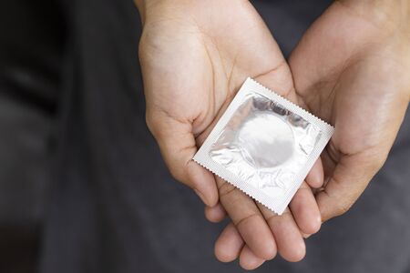 Woman hand holding and condom sitting on sofa background,protection, safe sex,contraceptive means.の写真素材