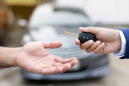 Close up of dealer giving key to new owner and shaking hands in auto show.auto business, car sale,...