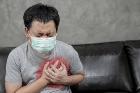 Thai young man wear face mask  having painful Chest having heart attack at home,Hands squeezing...