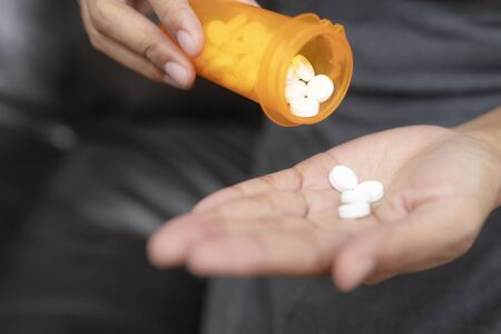 Close up of woman taking in pill she is pours the pills out of the bottle,taking painkiller to reduce sharp ache concept,health care and medicine concept.の写真素材