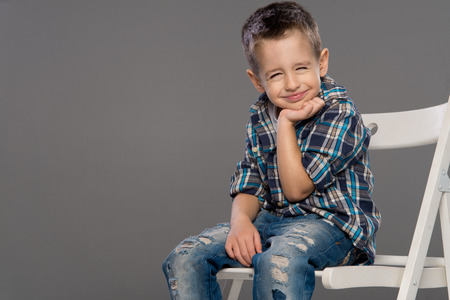 Casual boy with smile sitting om chair over a grey backgroundの写真素材