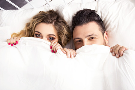 Young happy couple lying together in bedの写真素材
