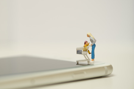 Miniature shopper standing on smart phone with cart ,easy to buy goods or services from a seller over the internet. Online shopping concept  with copy spaceの写真素材