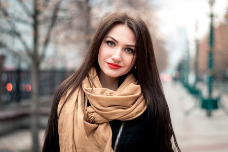 Autumn fashionable portrait of happy brunette young girl red lipstick outdoors in the cityの写真素材